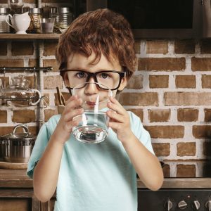 A young boy drinks from a glass of filtered tap water.