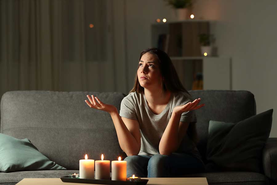 Woman sitting in dark living room with candles during a power outage