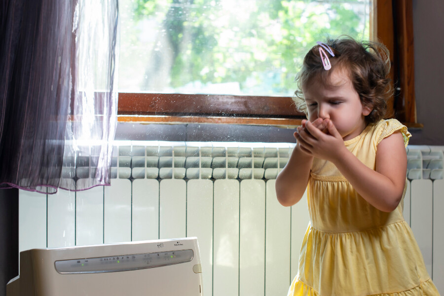 A little girl coughing and sneezing in her home due to poor indoor air quality.