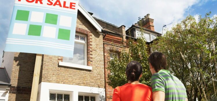 Excited couple envisioning their dream home for sale with 'For Sale' sign, thinking that once they purchase it they will be in need of reliable water softener companies in Austin TX to schedule a water test for their new water system.