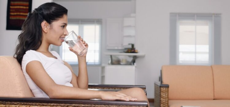 Woman sitting in a rattan chair and drinking a glass of nice Austin reverse osmosis water.