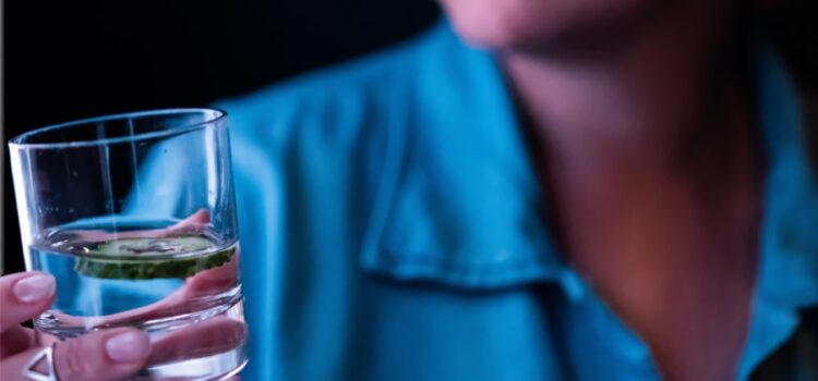 Close up of a woman in a blue shirt holding a glass of water from Round Rock water softener companies with a refreshing cucumber infusion