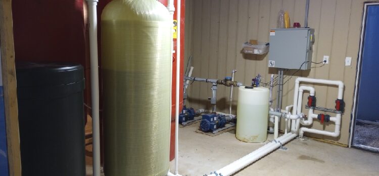 A water softener in a garage, surrounded by pipes and water tanks, efficiently purifies water.