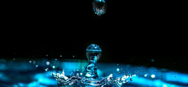 A vibrant blue drop of water splashing off the surface of water against a captivating black background – symbolizing the purity and effectiveness of reverse osmosis in Cedar Park.