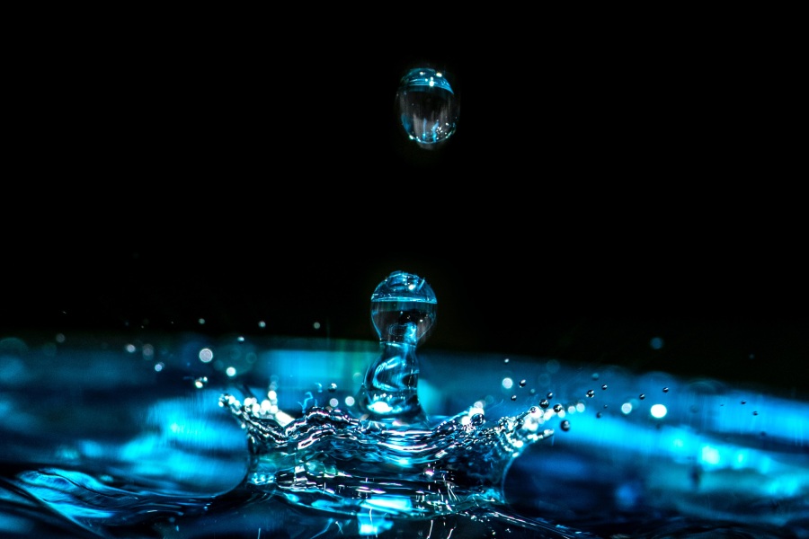 a blue drop of water splashing off the surface of water with a black background