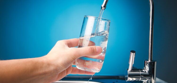 A person holding a glass of water from a faucet, emphasizing the importance of regular water softening system maintenance.