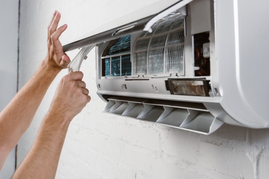 An image of technician's hands doing a cleaning routing to the air conditioner filter to avoid future dust allergies