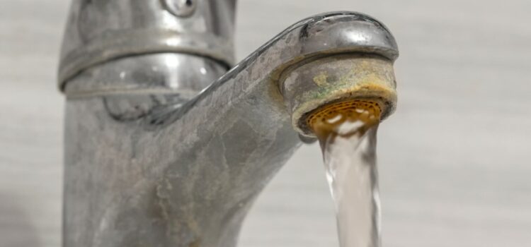 Rusty old tap aerator with hard water flowing through in Austin, highlighting the need for water treatment.