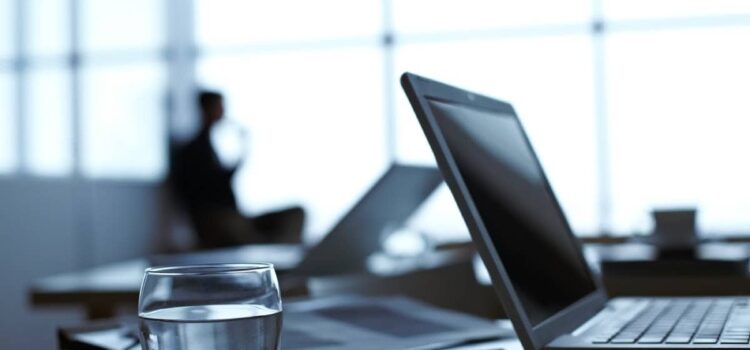 a glass of water over an office desk, next to a laptop