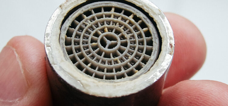 Hand holding a faucet aerator with hard water buildup – example of why regular water softener maintenance is important in Texas homes